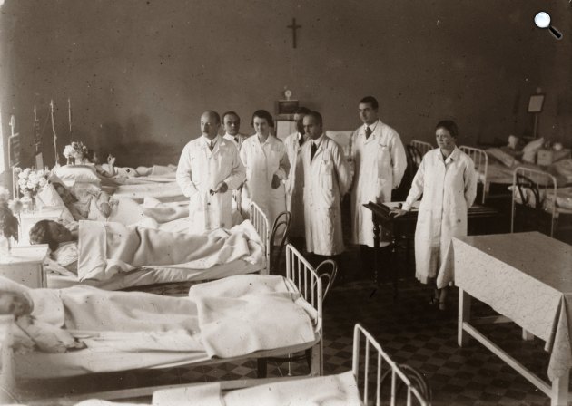 A Magyar Királyi Erzsébet Tudományegyetem Klinikájának kórterme, nagyvizit (ma Pécsi Tudományegyetem Klinikai Központ). Az orvoscsoport bal szélén dr. Ángyán János belgyógyász, egyetemi tanár női és férfi egyetemisták körében, 1928 (Fotó: Fortepan/POTE)